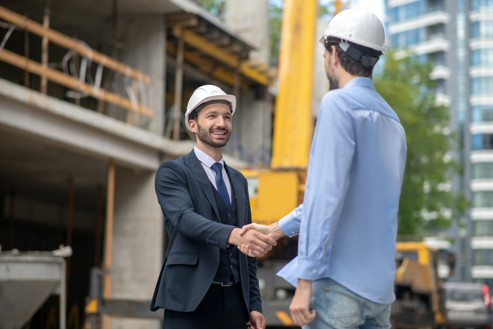 Building site. Building supervisor and foreman greeting, shaking hands with each other on building site
